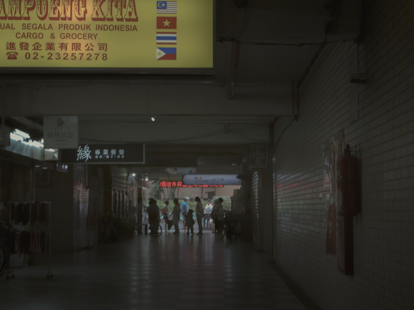 幕 騎樓牆上掛著印尼商店的黃色招牌，遠處有人走動
