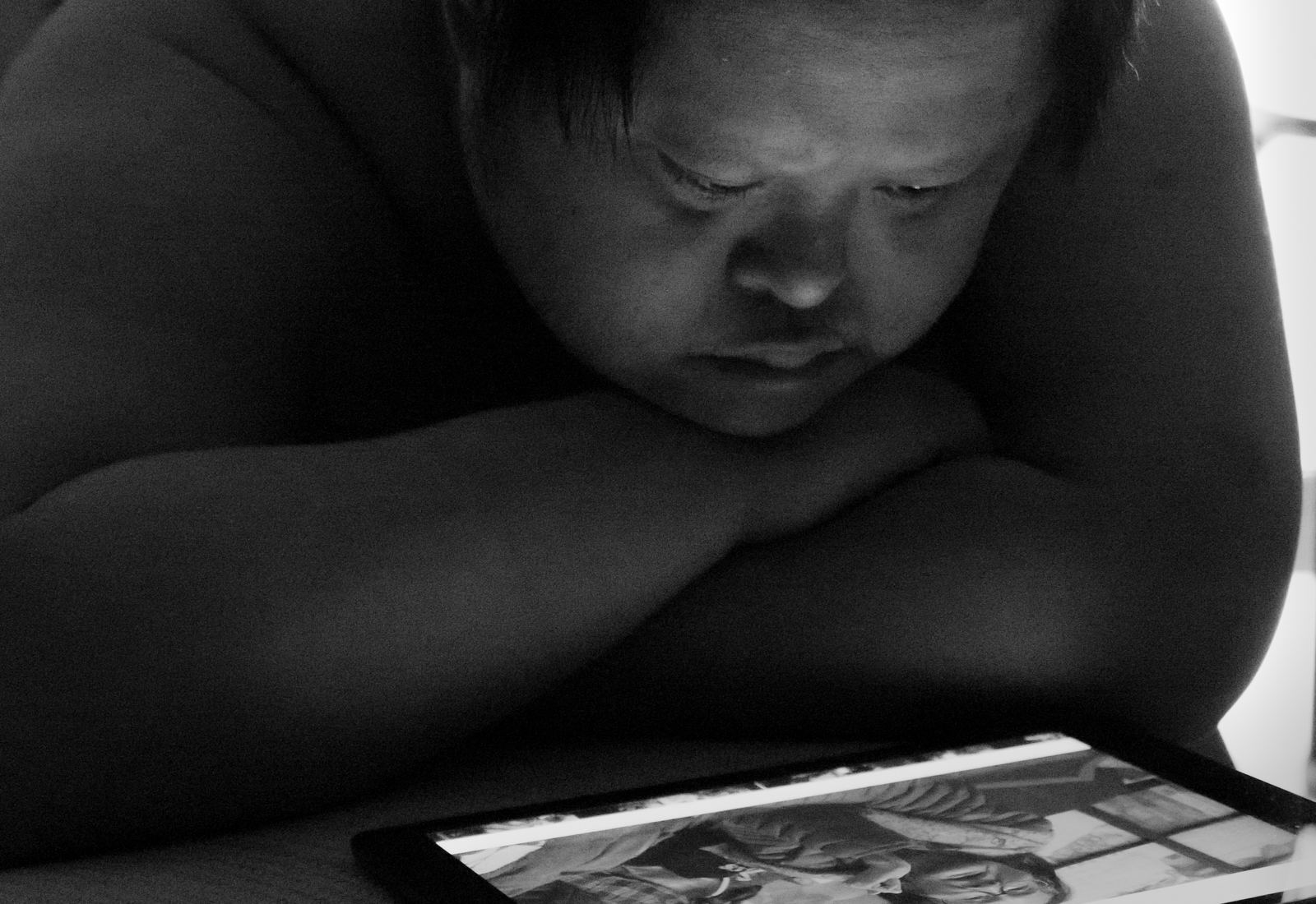 寍 男子趴在桌上凝視平板螢幕，光映在臉上