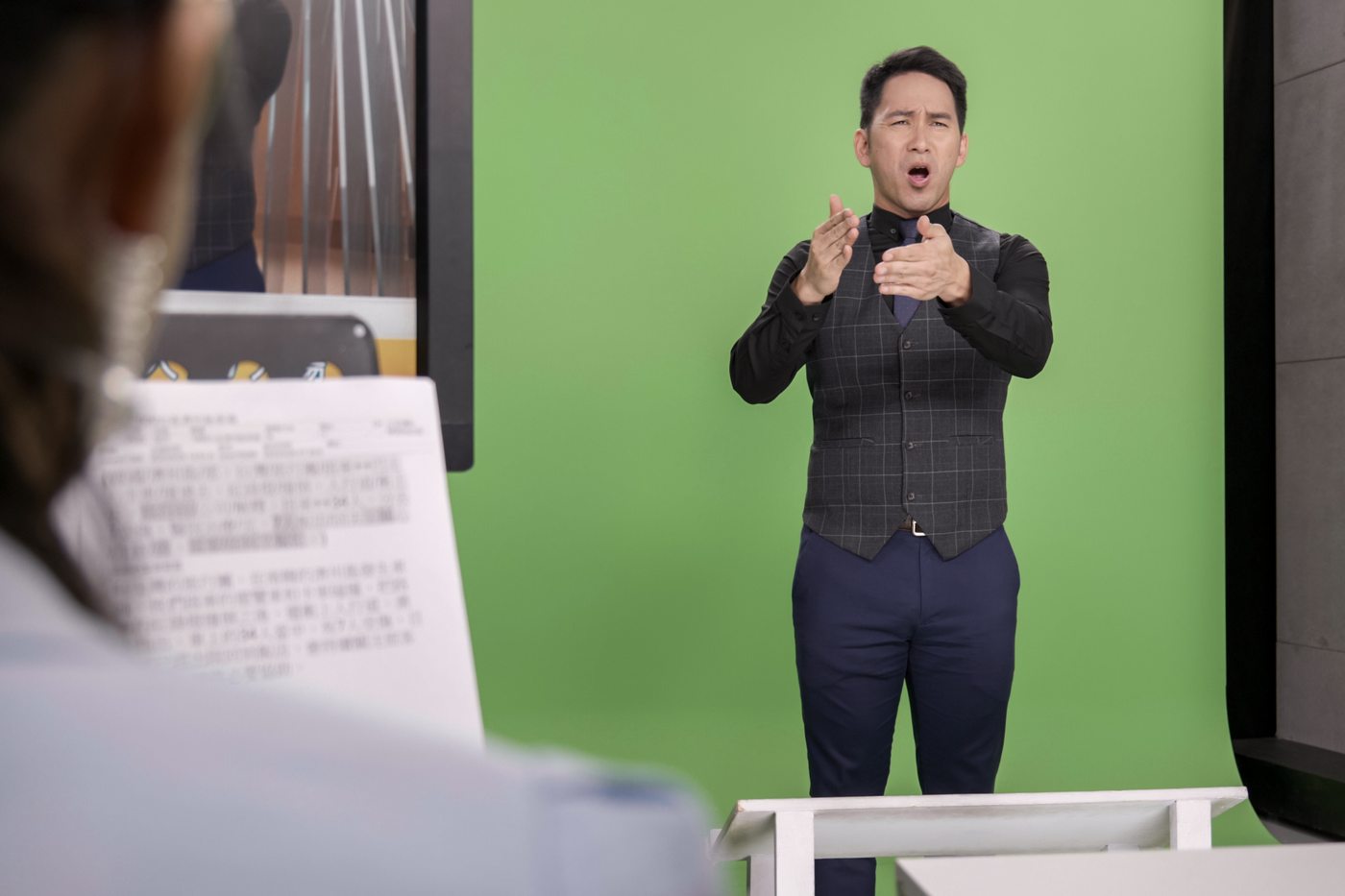 我是聾人 我的母語是手語 攝影棚綠幕前男子打著手語，前景是提詞資料