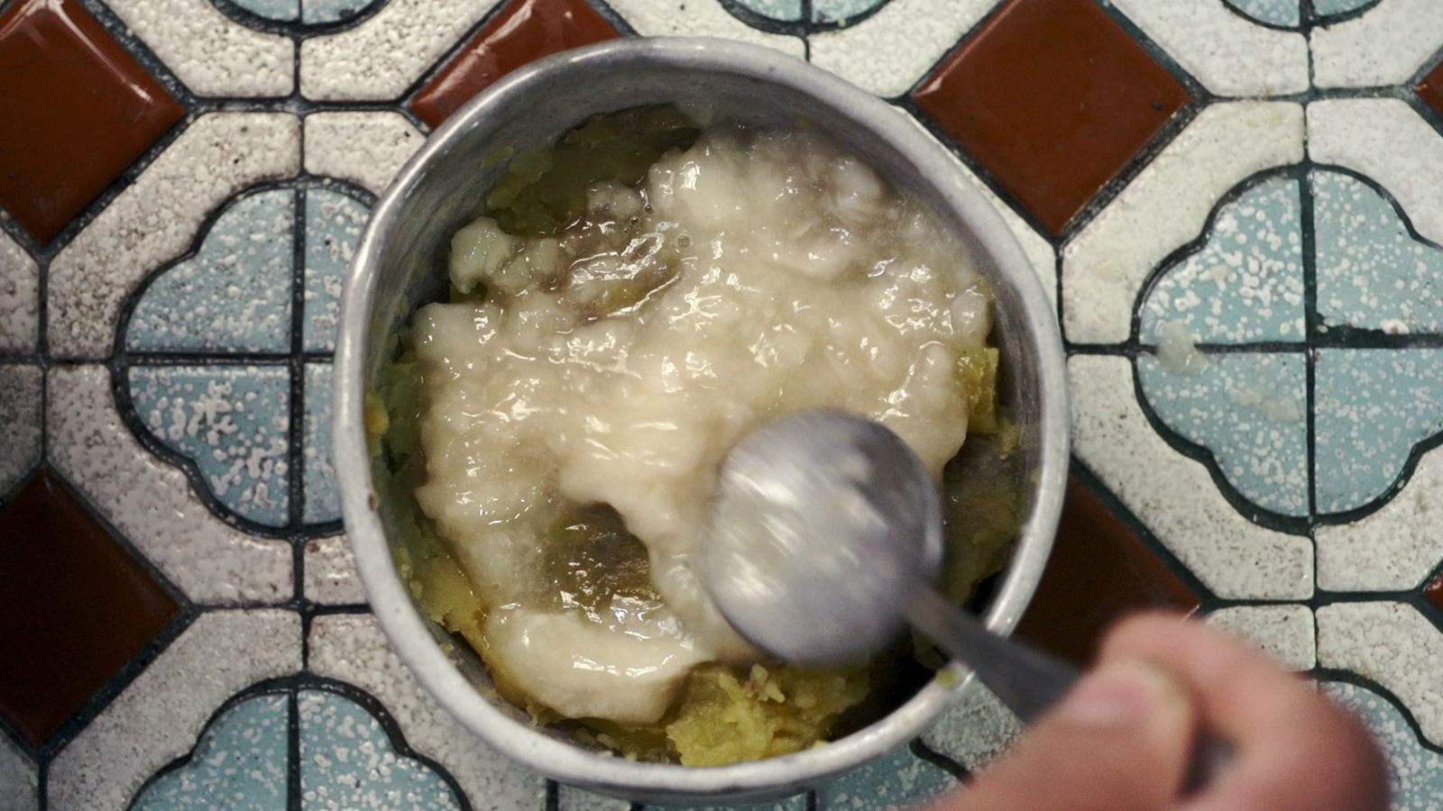 日出農東 花磚地上一只鋁鍋盛著熬煮的食物，有人以湯匙攪動