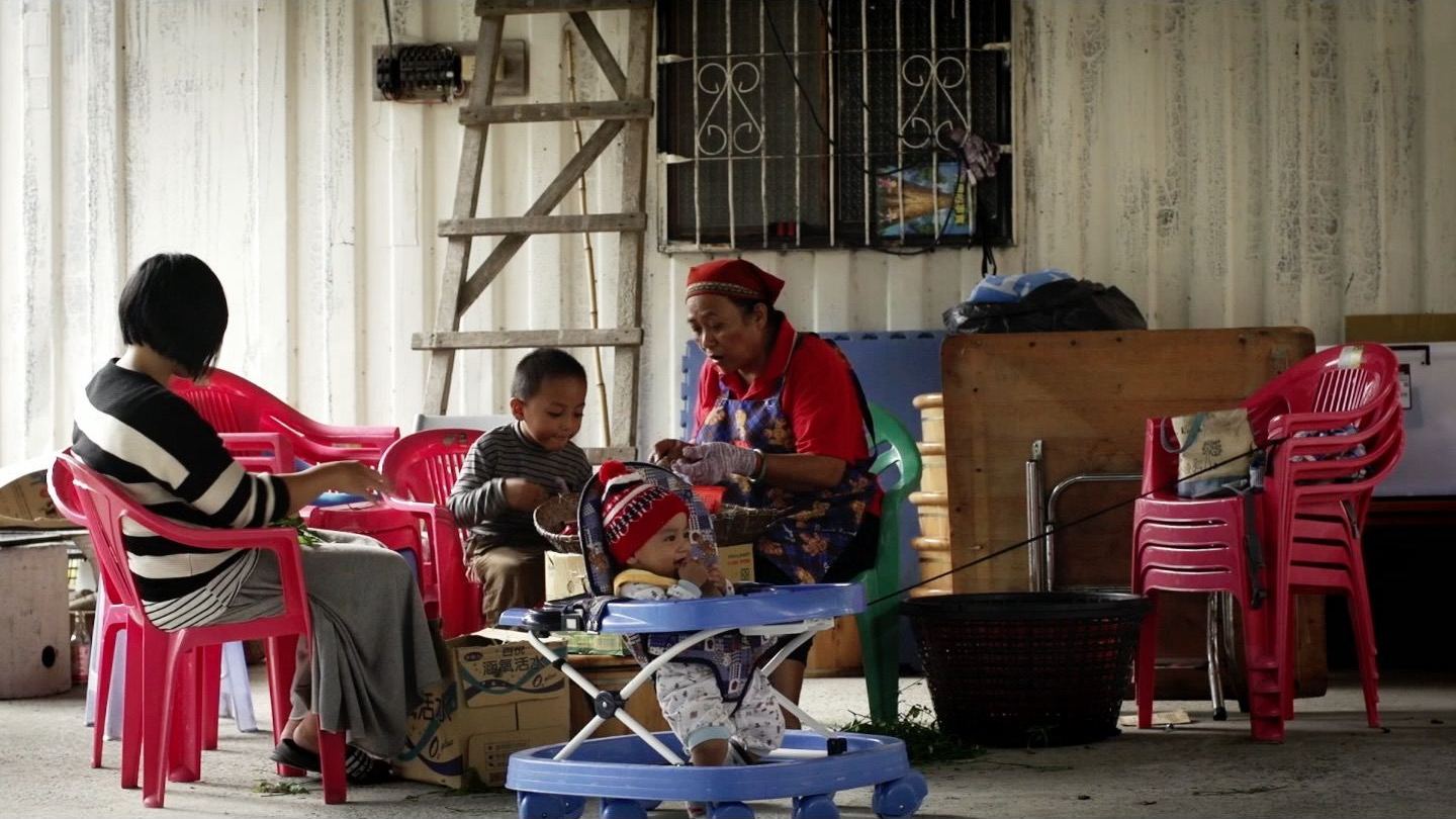 日出農東 鐵皮屋前一家人圍坐，孩子坐在學步車裡