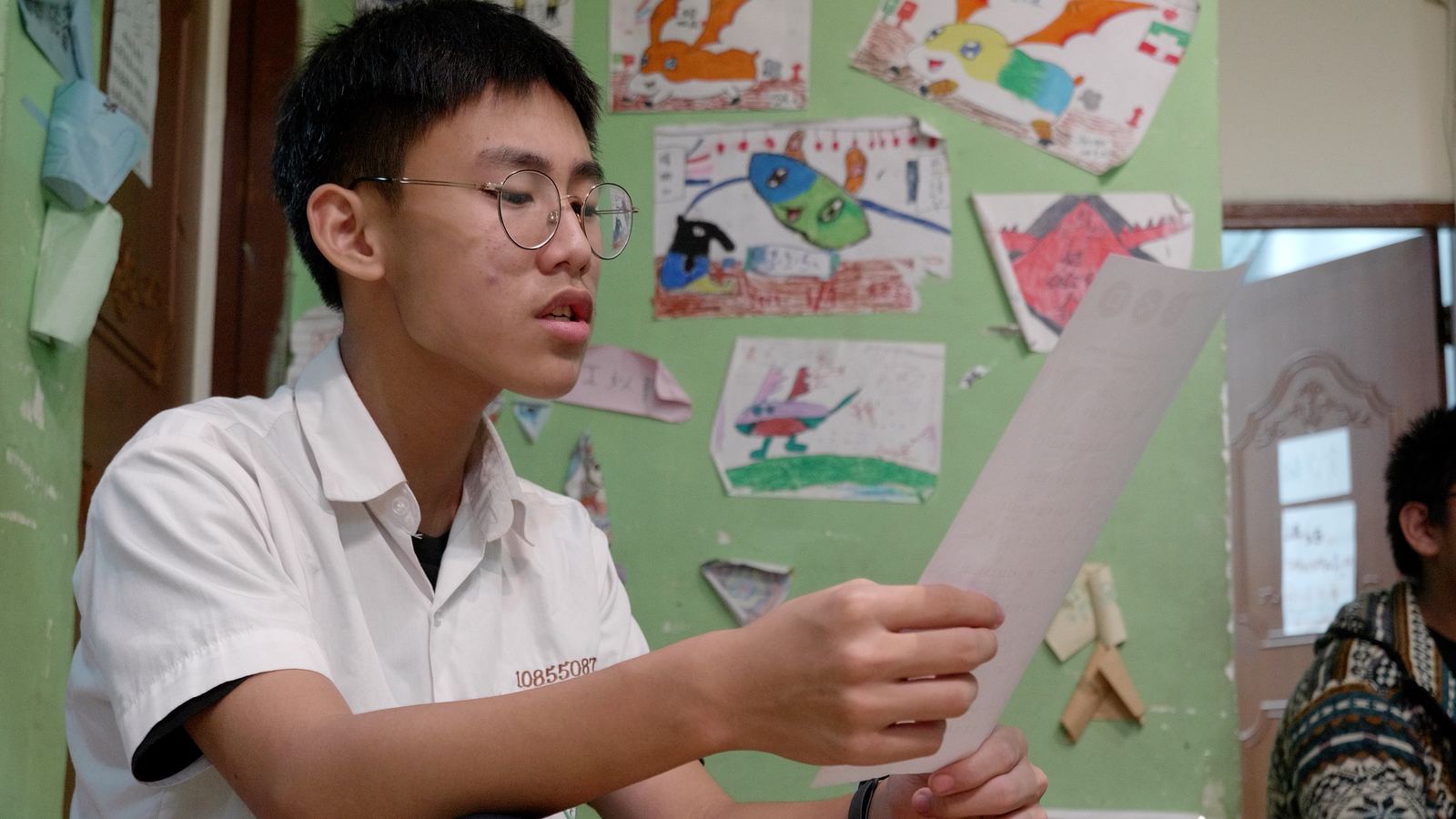 看見WAWA森林 戴眼鏡的少年在貼滿圖畫的教室裡讀著歌詞紙
